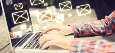 a person typing on a laptop with email icons coming out of the screen.