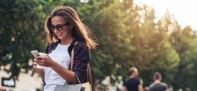a woman holding shopping bags and looking at her cell phone.